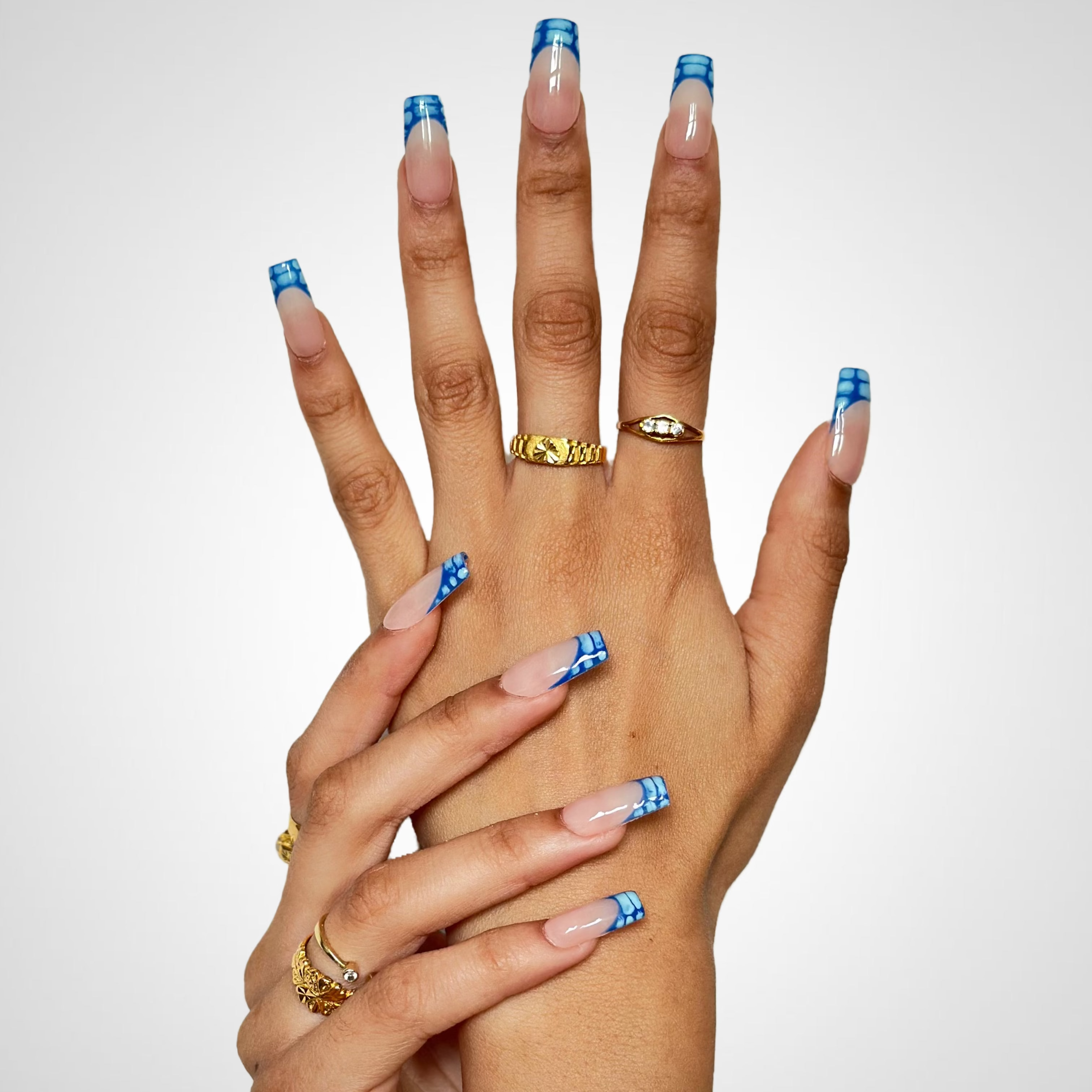 Two hands crossed together, showcasing long French-tip nails with a blue and light blue marble pattern.