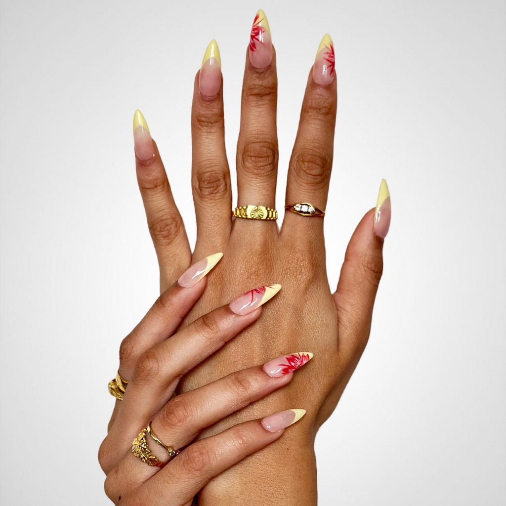 Two hands crossed together, showcasing long almond-shaped nails with a yellow-to-clear gradient and red floral designs.